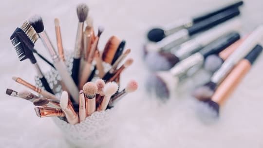 A brush holder displays various cosmetic brushes on a counter. Several more are blurred in the background.