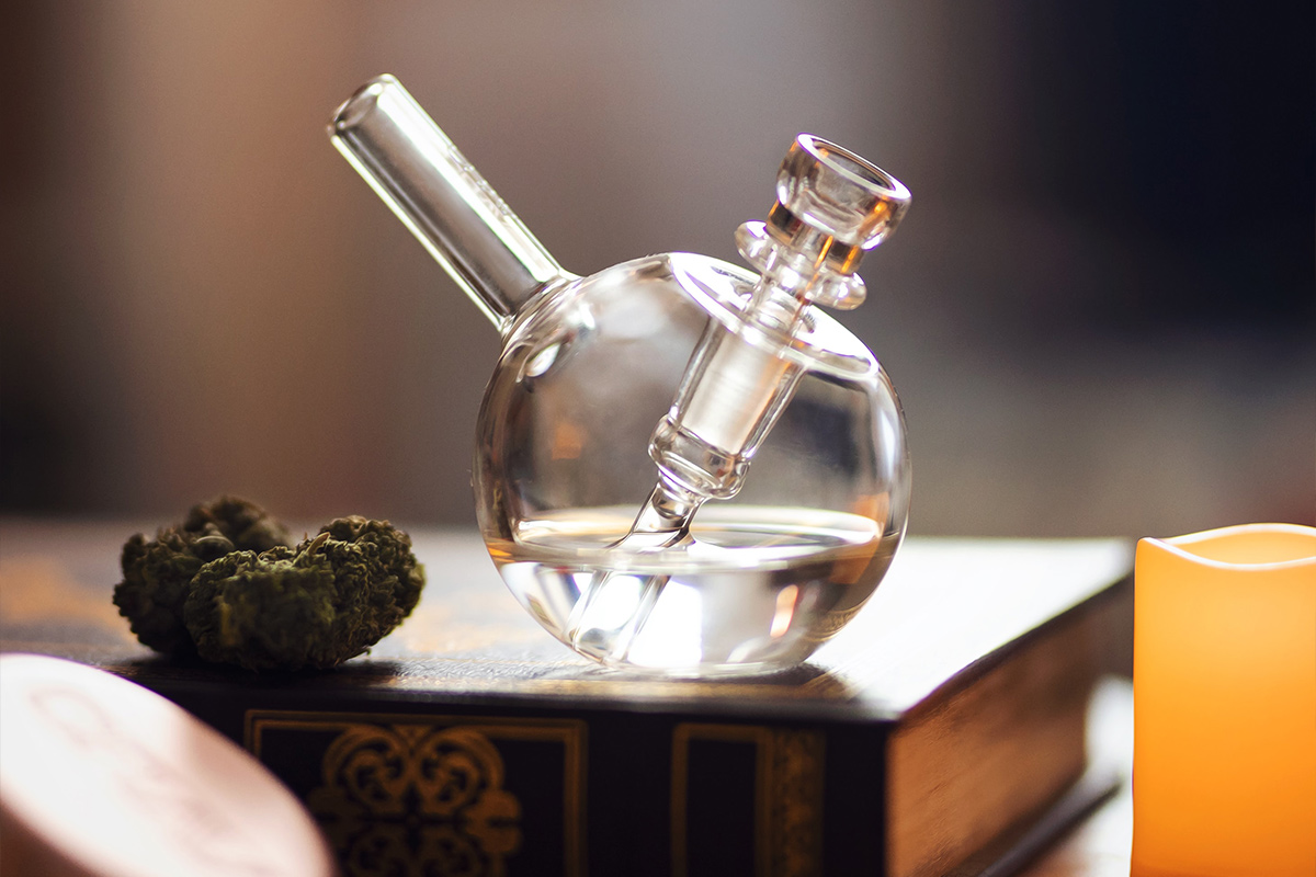 A bubbler and a nugget of cannabis rest tastefully on a book having been sold with cannabis crop & dispensary insurance