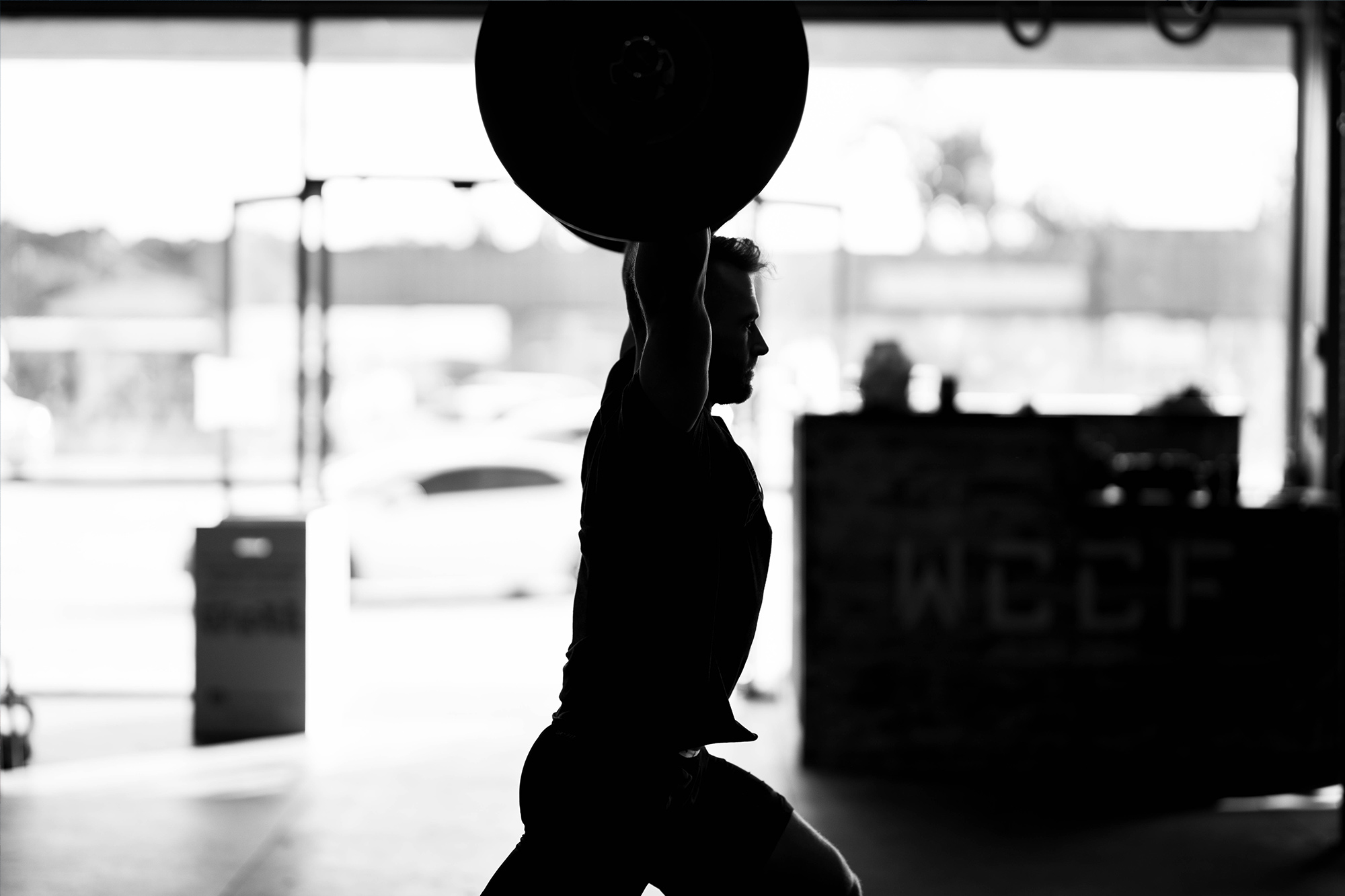 A crossfitter lifts a barbell high with excellent form. His coach has trained him well with crossfit trainer insurance.