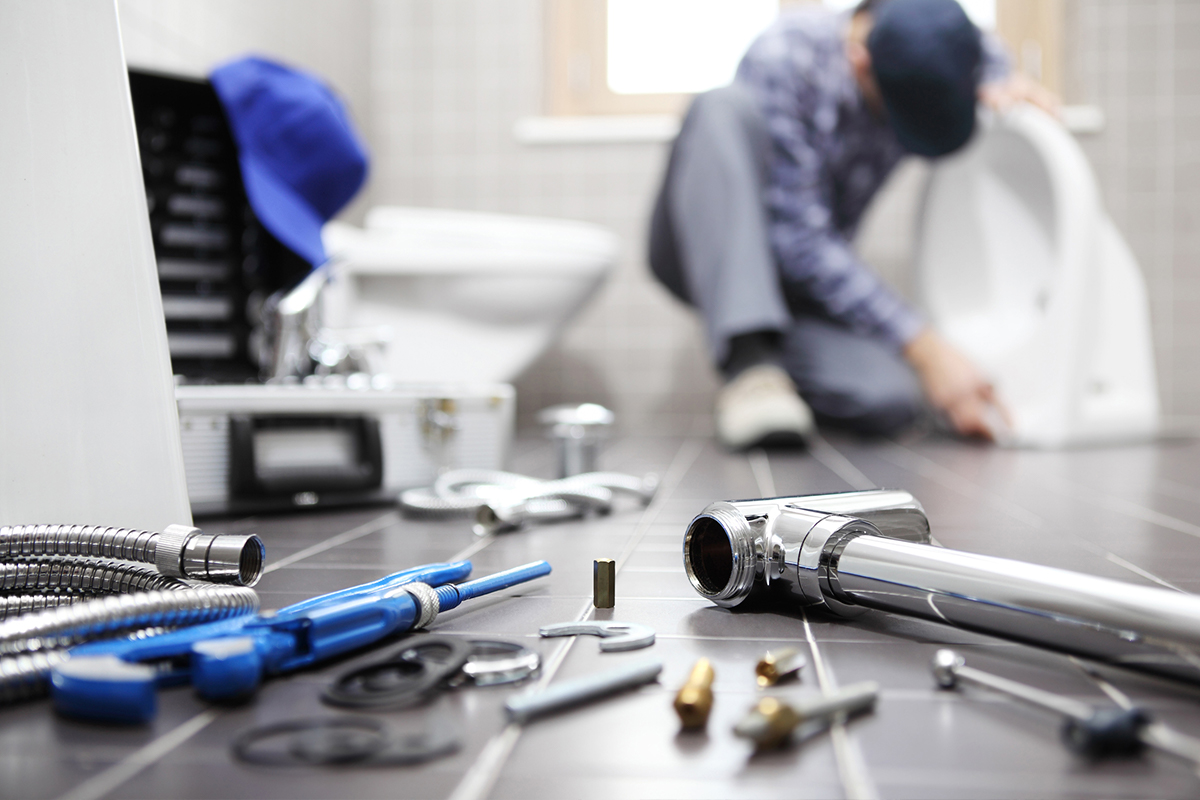 A plumber works in the background on a toilet. His tools are in-focus near the camera.
