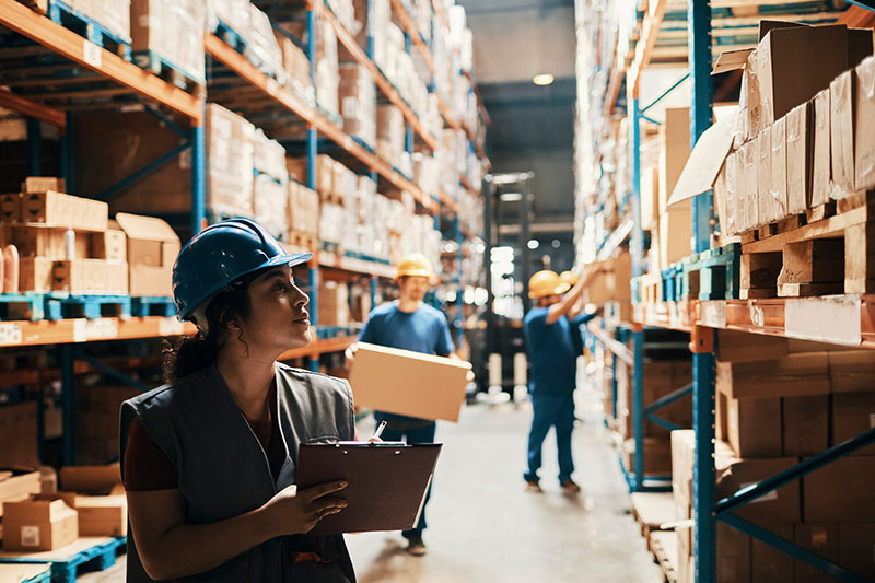 An woman in a hardhat and vest inspects a warehouse for safety.